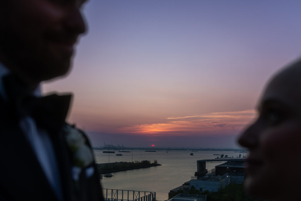 Two tuxedoed silhouettes framing a pink and orange sunset over the water