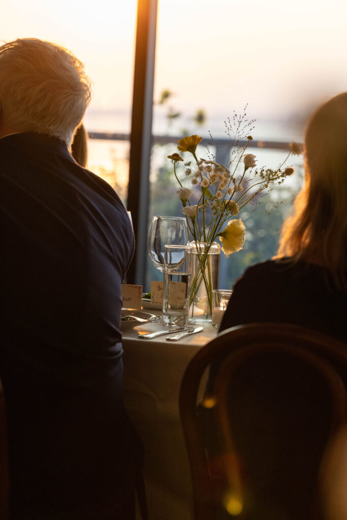 Two guests seated by a window at sunset with a wildflower arrangement on the table
