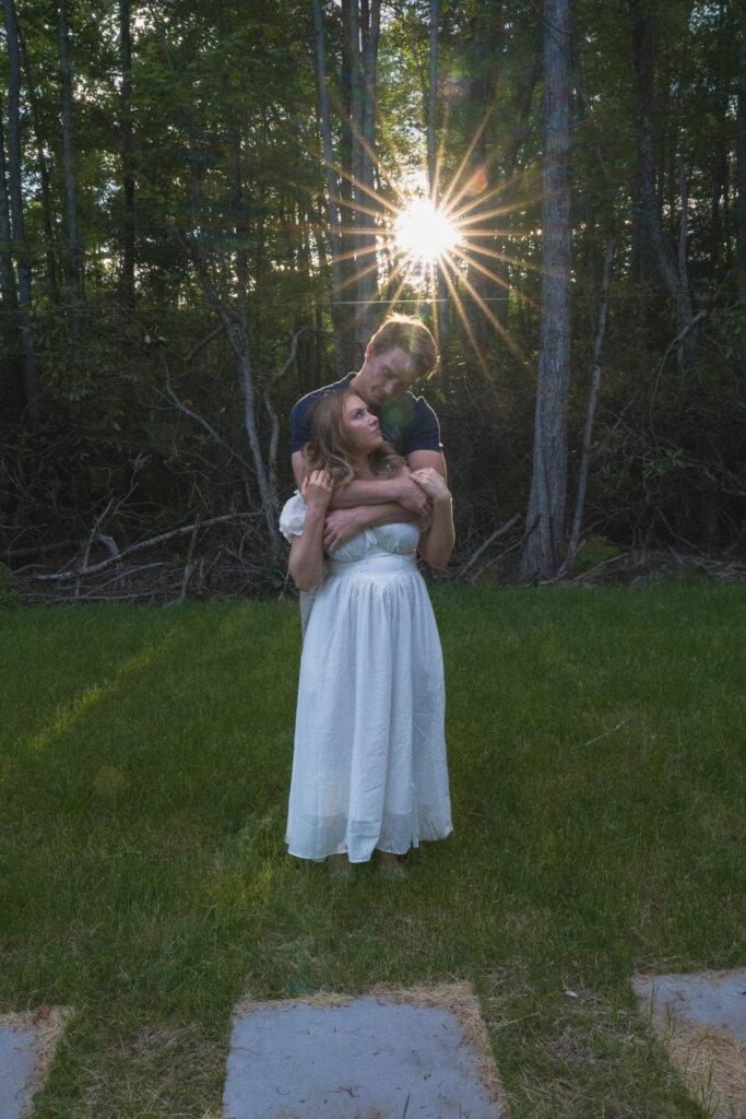 Couple embracing in the woods with a golden sunburst breaking through the trees
