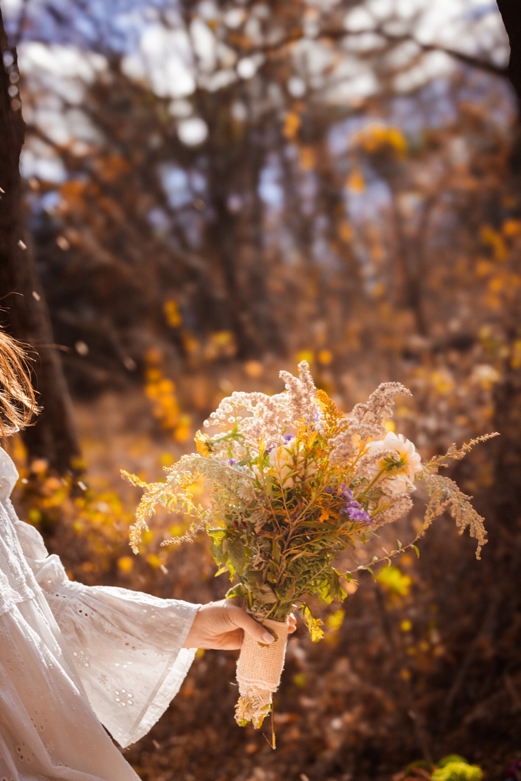 Bride holding a wildflower bouquet against warm autumn foliage