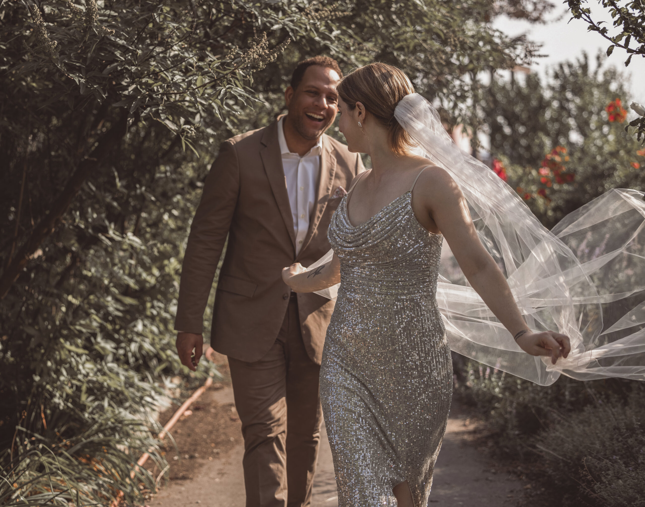 Couple walking hand in hand outdoors as the bride’s veil catches the wind