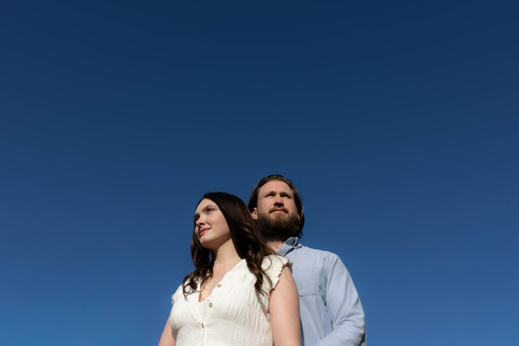 Engaged couple photographed from below against a deep blue sky
