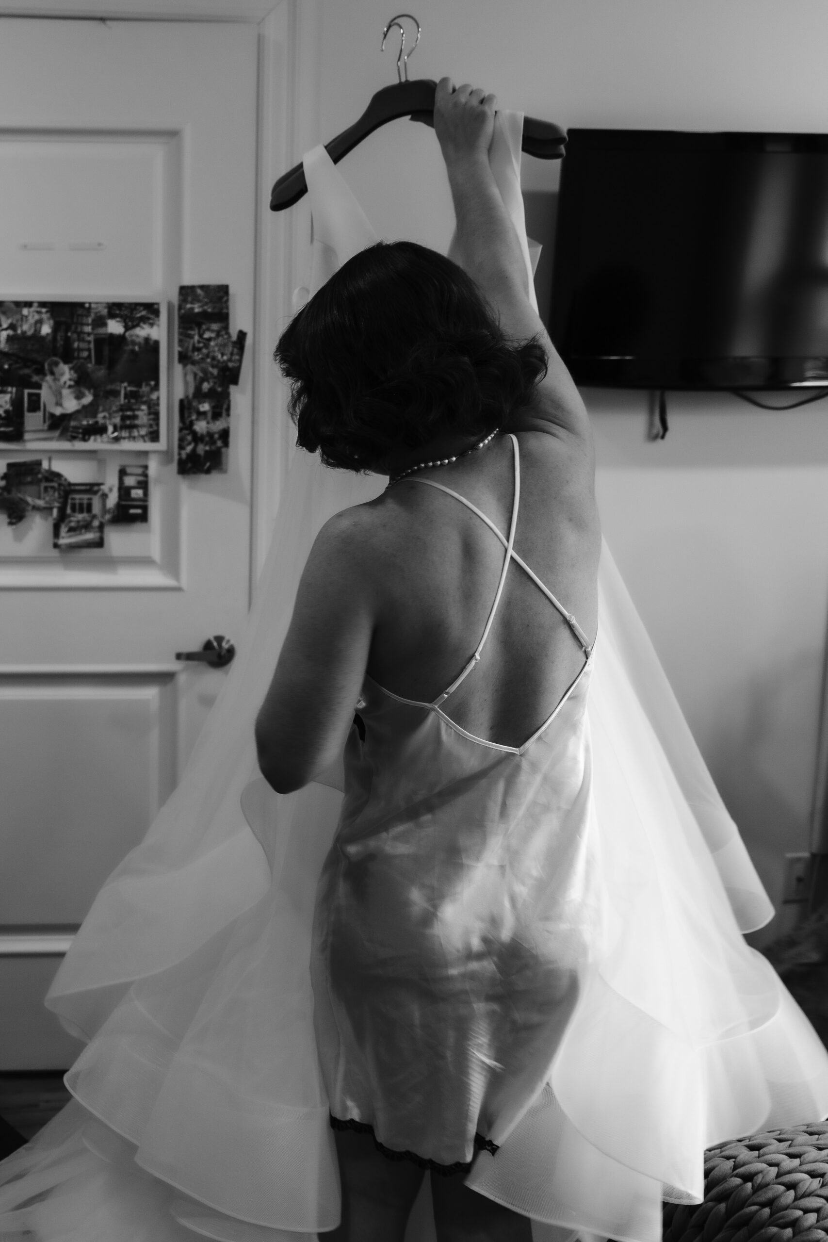 Black and white photo of a bride in an open-back gown getting ready before the ceremony