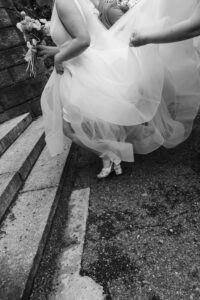 Black and white detail of a bride's gown and shoes on stone steps