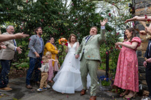 Wedding guests cheering for the newlyweds at an outdoor garden ceremony