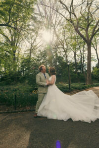 Couple embracing in a sunlit park with the bride's gown train spread across the grass