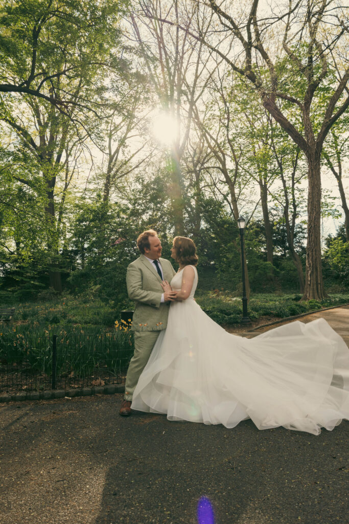 Couple embracing in a sunlit park with the bride's gown train spread across the grass