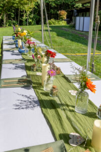 Long outdoor reception table set with wildflower bud vases on a green lawn